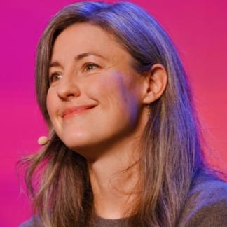 Portrait of Paige smiling softly with a microphone, giving a talk